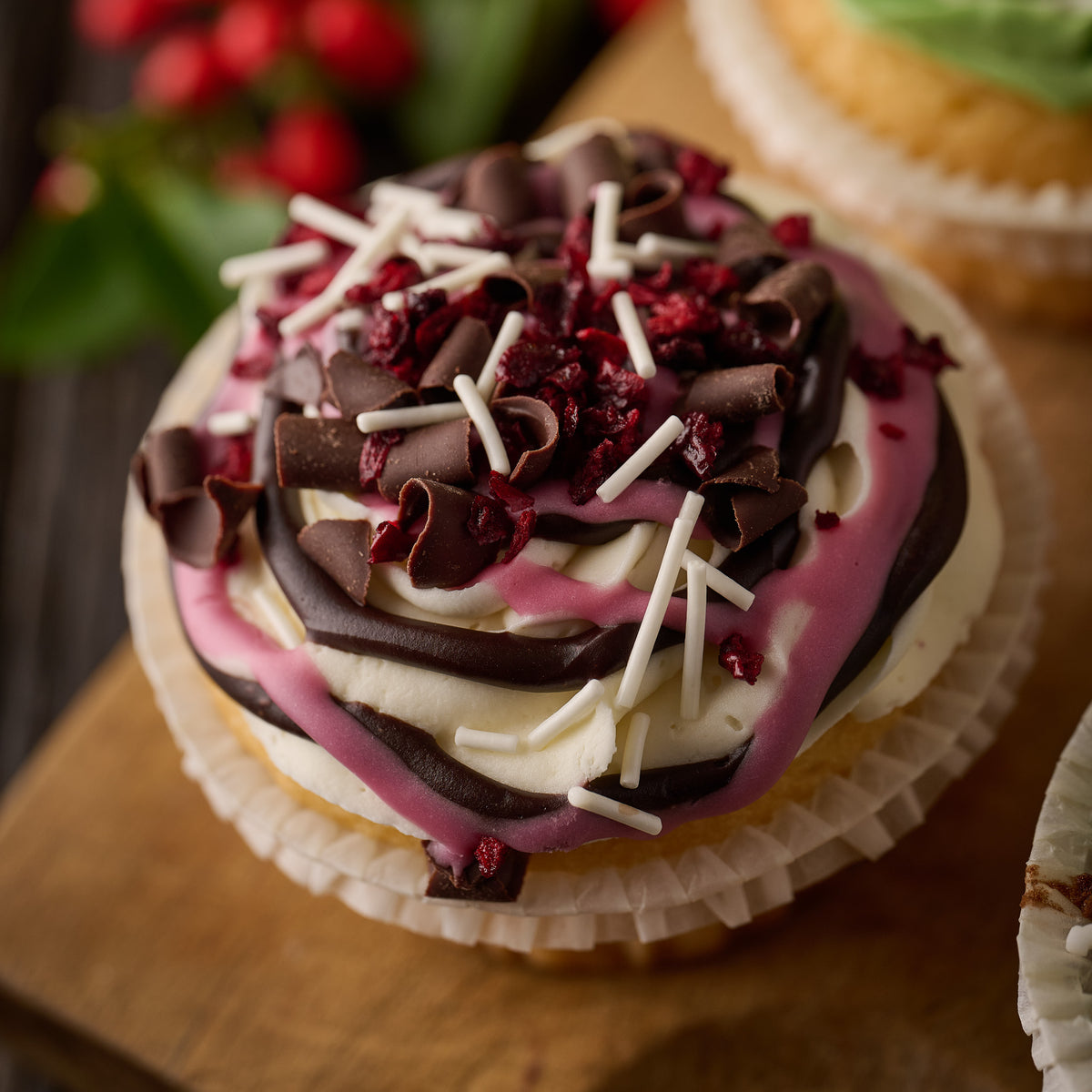a chocolate and cherry cupake topped with cream cheese frosting finished with chocolate drizzles, candies cherries and dark chocolate curls