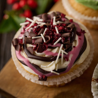 a chocolate and cherry cupake topped with cream cheese frosting finished with chocolate drizzles, candies cherries and dark chocolate curls