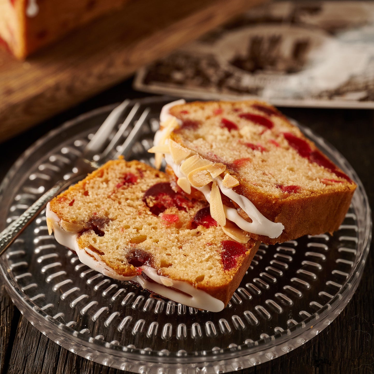 slices of cherry bakewell loaf cake on plate showing almond sponge with cherries, raspberry jam icing and flaked almonds