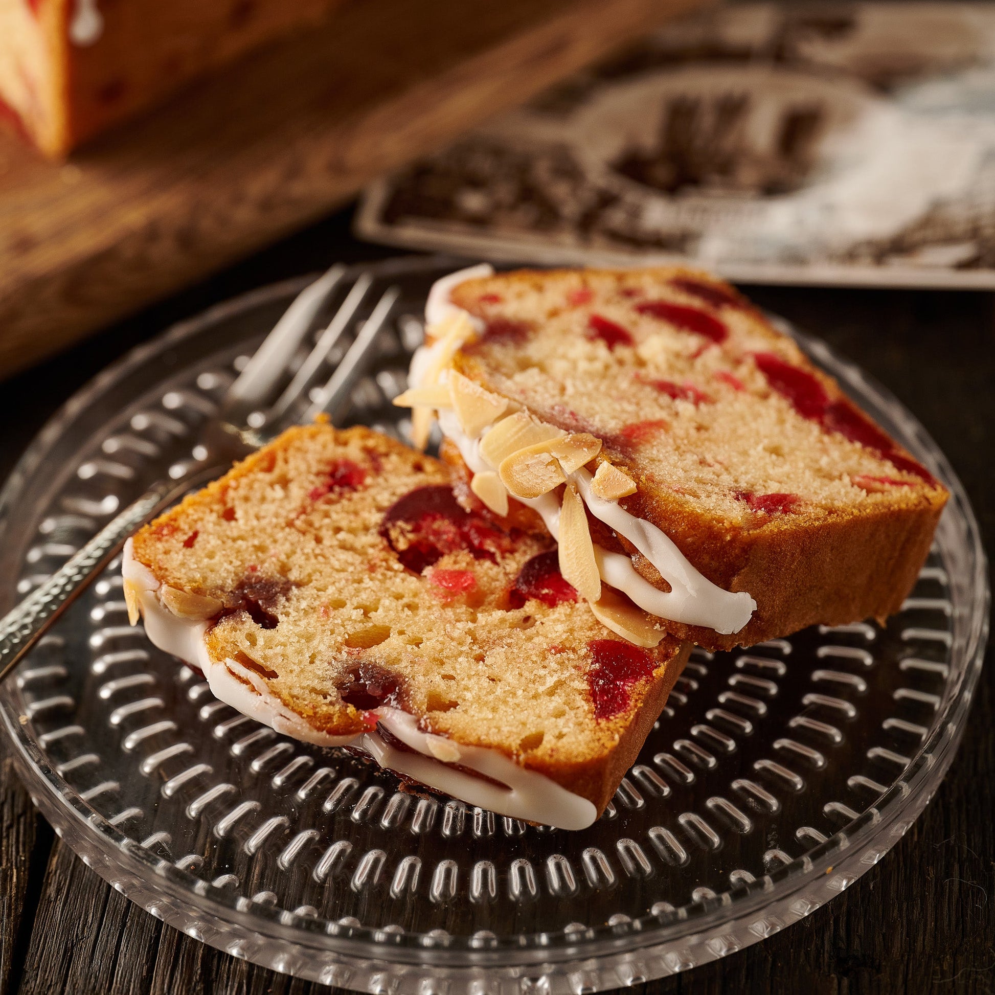 slices of cherry bakewell loaf cake on plate showing almond sponge with cherries, raspberry jam icing and flaked almonds
