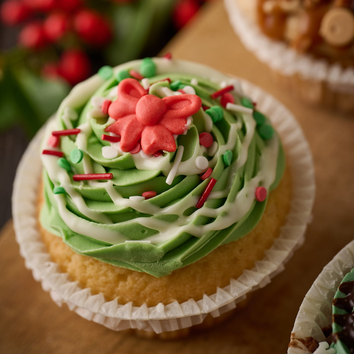 cupcake topped woth green frosting, white chocolate drizzle, festive sprinkles and finished with a red sugar bow. 
