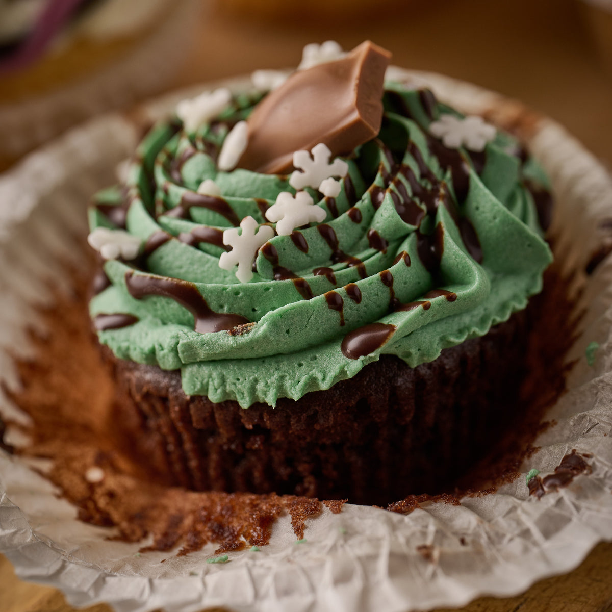 chocolate cupcake topped with mint frosting, chocolate drizzle, sugar snowflakes and a chunk of galaxy mint chocolate 