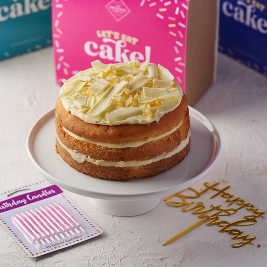 A triple-layered St. Clements Cake with lemon and orange sponge, baked with citrus peel, and layered with orange frosting and lemon curd with a pack of birthday candles and 'Happy Birthday' cake topper.