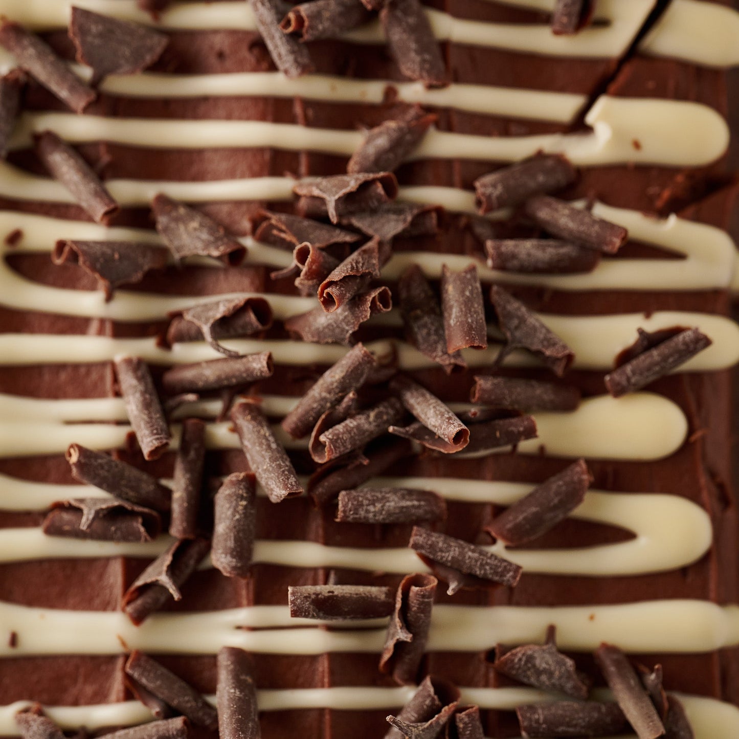 close up triple chocolate loaf cake topping with chocolate frosting, white chocolate drizzle and dark chocolate curls