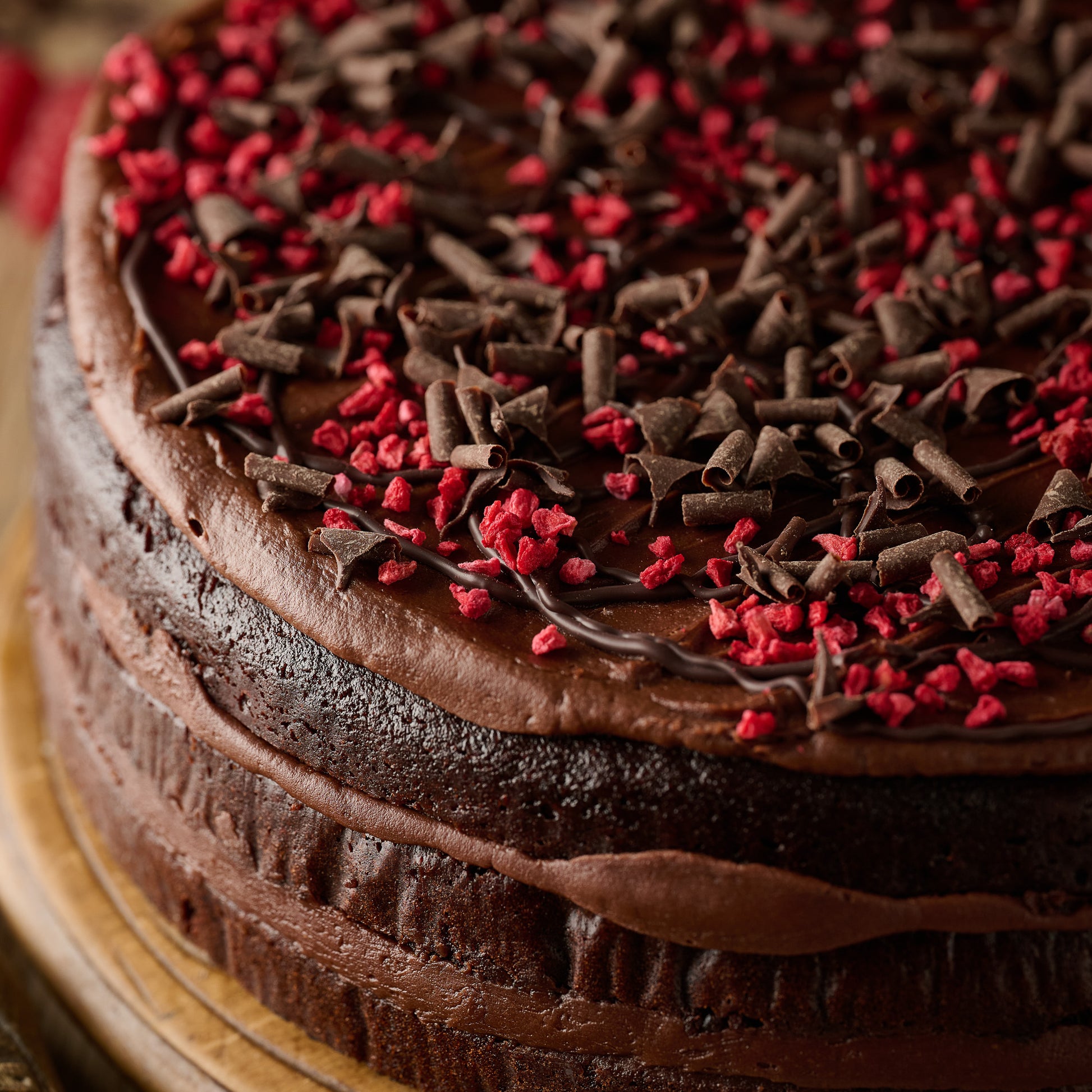 vegan chocolate raspberry cake close up with chocolate sponge, frosting, dark chocolate curls and freeze dried raspberries 
