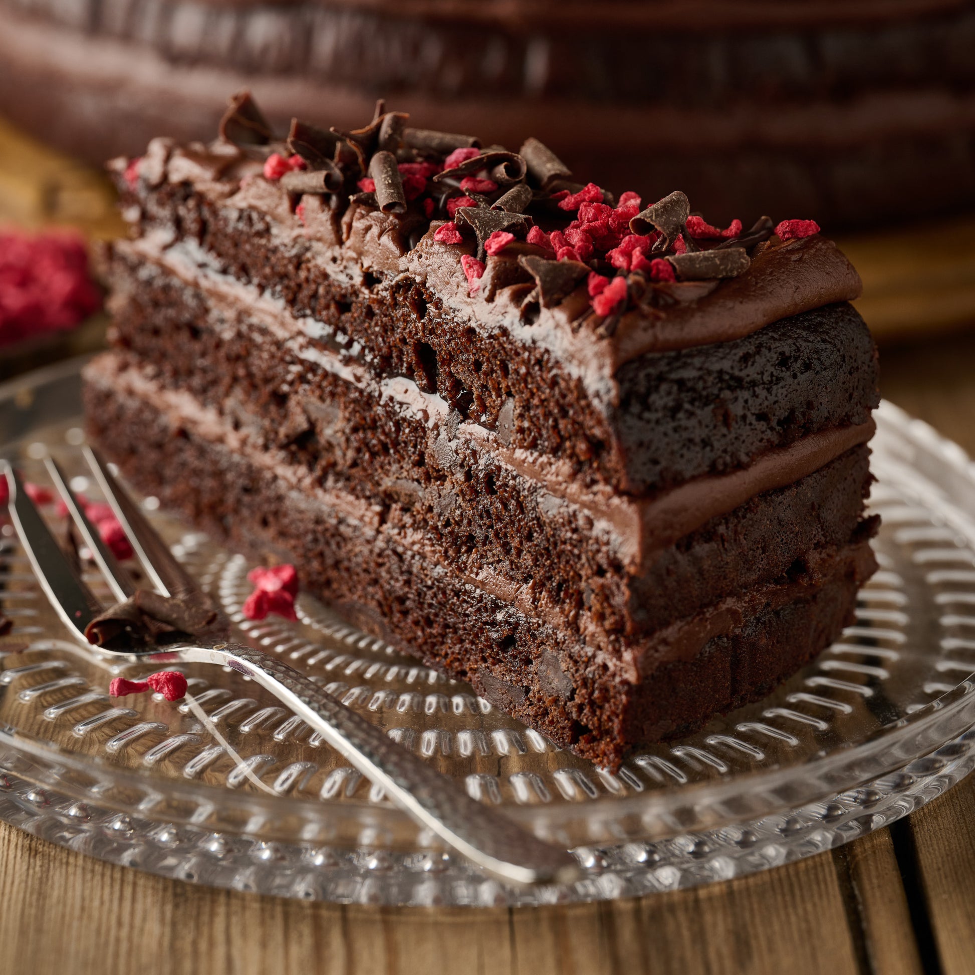 Slice of vegan dark chocolate and raspberry cake showing chocolate sponge, frosting and raspberry jam filling