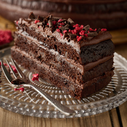 Slice of vegan dark chocolate and raspberry cake showing chocolate sponge, frosting and raspberry jam filling